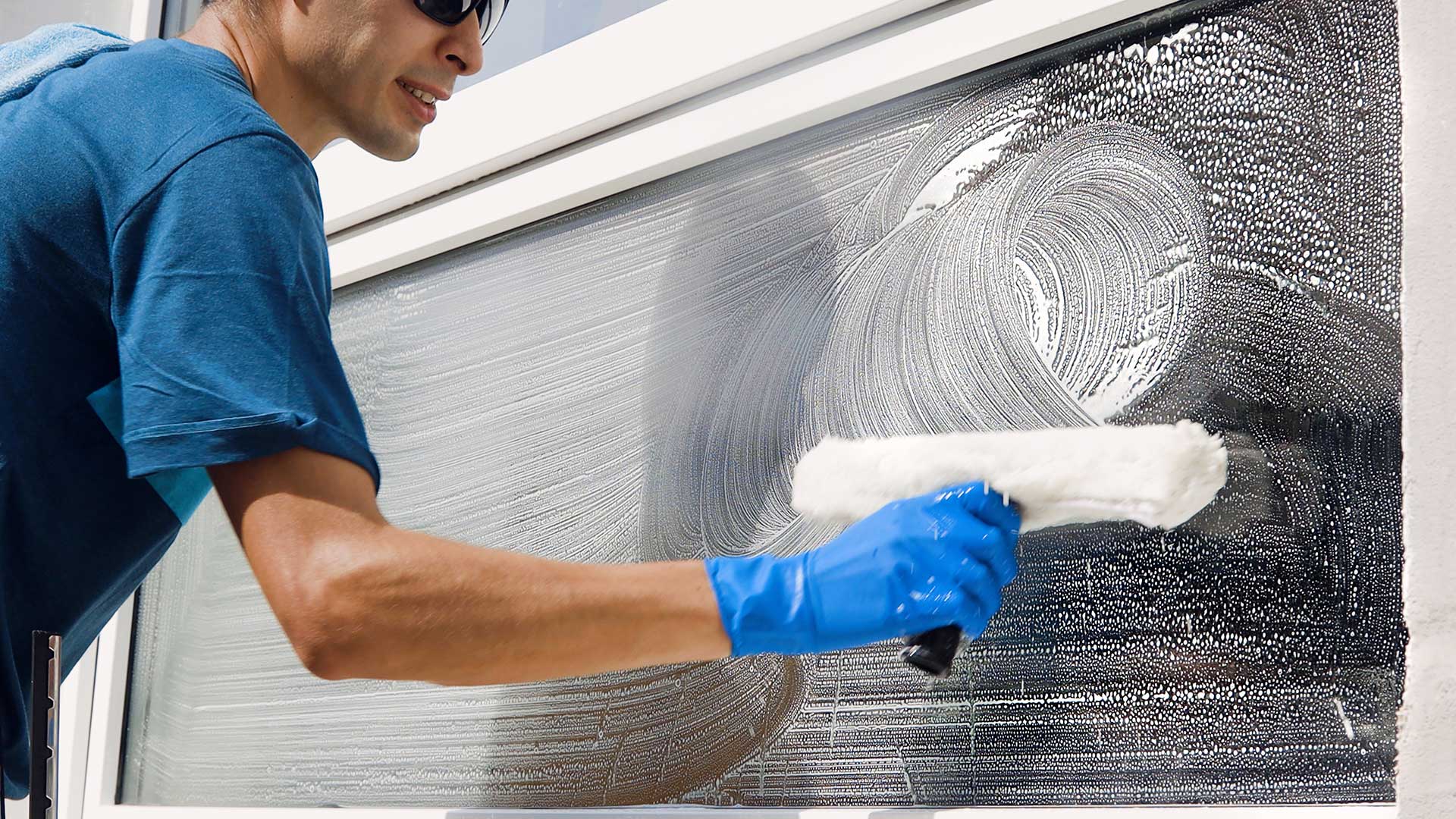 Ein Mann mit Sonnenbrille und blauen Handschuhen putzt ein Fenster
